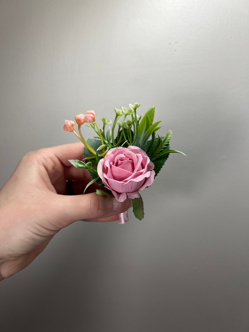 May include: A pink rose boutonniere with greenery and small pink buds.