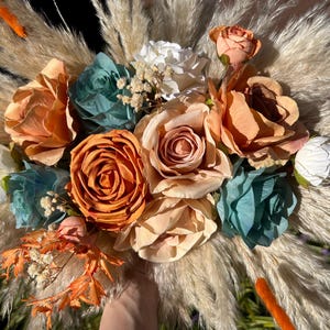 Op de afbeelding: Een boeket gedroogde bloemen met een mix van perzik-, oranje- en witte rozen, blauwe en groene succulenten en gedroogd pampasgras.