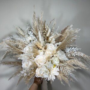 Può includere: Un bouquet da sposa bianco e beige con erba della pampa, rose bianche e altri fiori secchi.