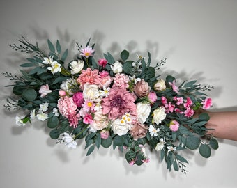 May include: A large bouquet of pink, white and blush-coloured artificial flowers with greenery. The bouquet is arranged in a cascading style and features a variety of flower types, including roses, dahlias and carnations.