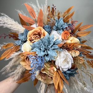 May include: A bouquet of faux flowers in shades of peach, white, and blue with dried pampas grass and brown foliage.