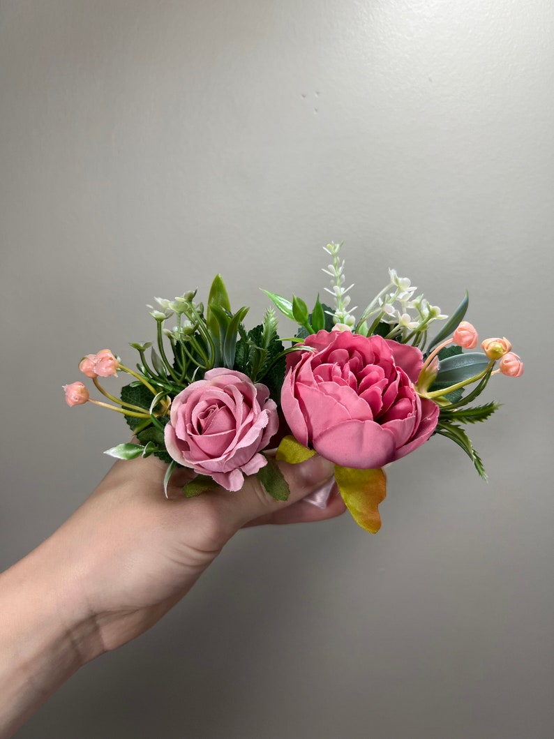 May include: A bouquet of pink and white artificial flowers with green leaves. The flowers are arranged in a hand.