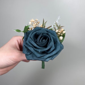 May include: A dark green rose with small white and beige flowers and green leaves.