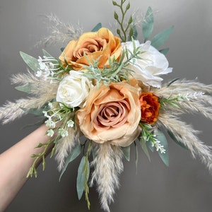 May include: A bouquet of peach and white roses with dried pampas grass and greenery.