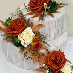 May include: Two-tiered faux cake decorated with orange, white and green silk flowers and autumn-coloured leaves.