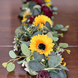 May include: A garland with burgundy and yellow flowers, green leaves, and white berries. The garland is perfect for adding a touch of fall to your home decor.