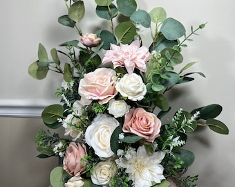 May include: A wedding centerpiece featuring a variety of artificial flowers in shades of pink and white, including roses, dahlias, and eucalyptus greenery.