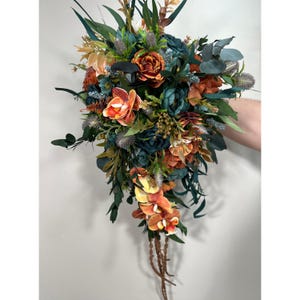 May include: A cascading bridal bouquet with teal and orange flowers. The bouquet features orchids, roses, and greenery.