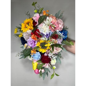 May include: A colourful bridal bouquet featuring a variety of flowers, including sunflowers, roses and daisies. The bouquet is tied with a white ribbon and has a cascading design.