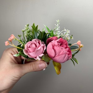 May include: A pink and green floral arrangement with two pink roses and greenery.