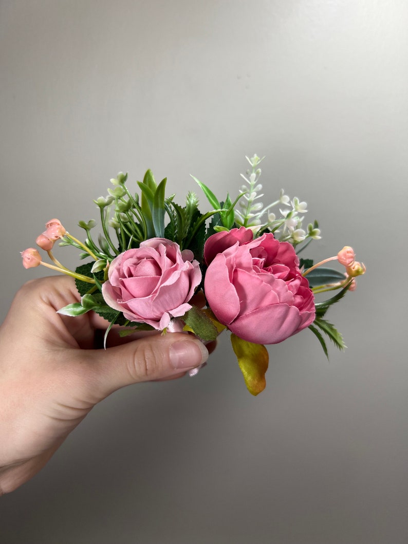 May include: A pink and green floral arrangement with two pink roses and greenery.
