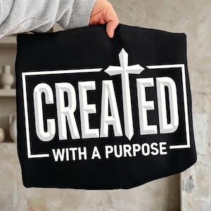 Peut inclure: Tissu noir avec l'inscription blanche "CREATED WITH A PURPOSE" dans un cadre rectangulaire blanc. Une croix blanche est centrée au-dessus du mot "CREATED".