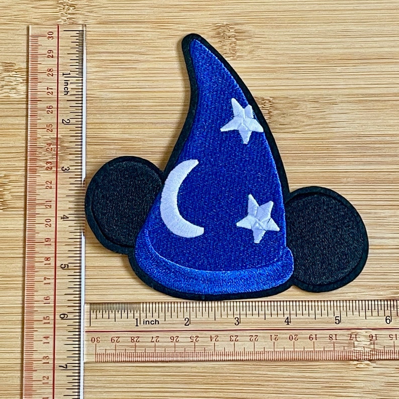 May include: Blue felt embroidered patch of Mickey Mouse's head wearing a blue sorcerer hat with white stars and a crescent moon. The patch is approximately 3 inches wide.