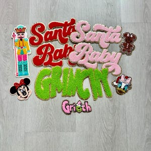 May include: A collection of embroidered patches with holiday and cartoon themes. Includes patches with the words "Santa Baby" and "Grinch", along with images of a nutcracker, Minnie Mouse, a gingerbread bear, and Daisy Duck.