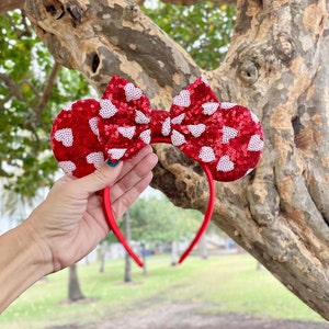May include: Red and white heart-shaped headband with a bow. The headband is made of sequins and is perfect for a Valentine's Day party.