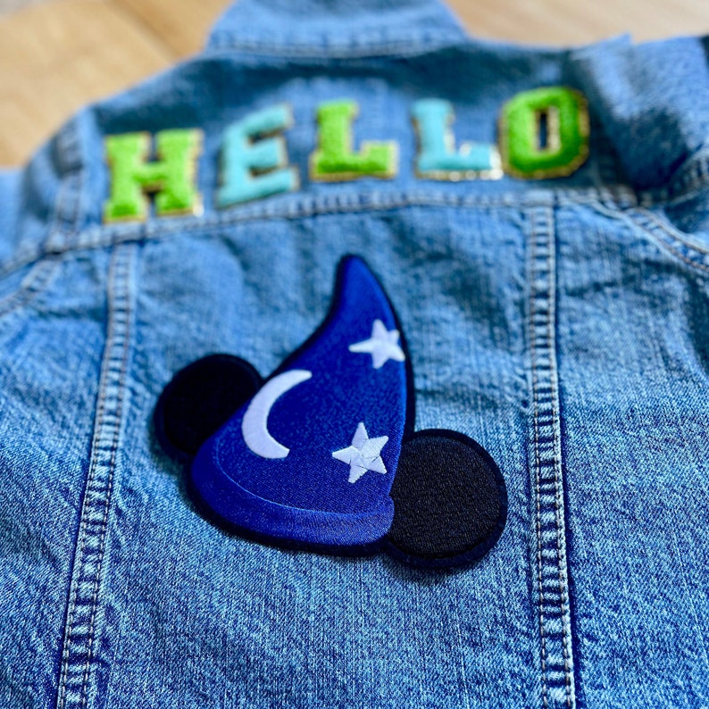 May include: A blue denim jacket with a blue and black Mickey Mouse sorcerer hat patch and the word "HELLO" in green and blue letters on the back.