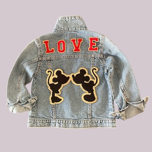 May include: A light blue denim jacket with a black and gold Mickey Mouse couple silhouette patch and the word "LOVE" in red letters on the back.