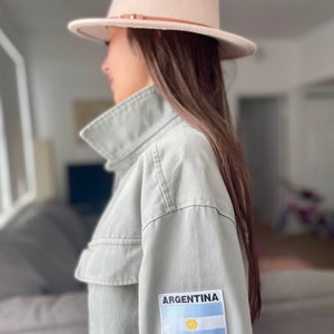May include: A light green utility jacket with a patch on the sleeve that says "ARGENTINA" and features the Argentinian flag.