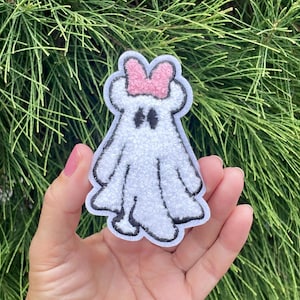 May include: White ghost with a pink bow on its head. The ghost has black eyes and a fuzzy texture.