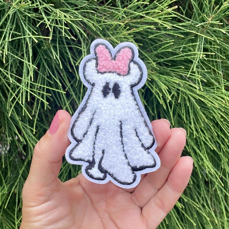 May include: White ghost with a pink bow on its head. The ghost has black eyes and a fuzzy texture.