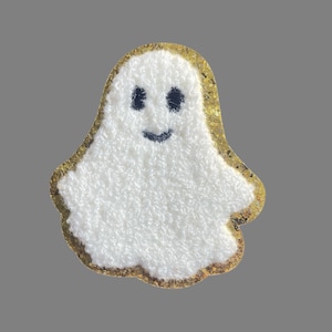 May include: A white fuzzy ghost with a black smiling face and eyes. The ghost is outlined in gold glitter.