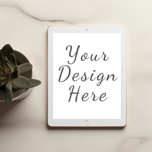 May include: A white tablet with a gold-colored frame displays the text "Your Design Here" in a stylish script. A small succulent plant in a white pot sits to the left of the tablet on a marble surface.