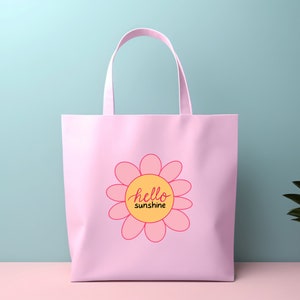 Op de afbeelding: Roze tote bag met een roze bloemetjesontwerp en de tekst "hello sunshine" in een gele cirkel.