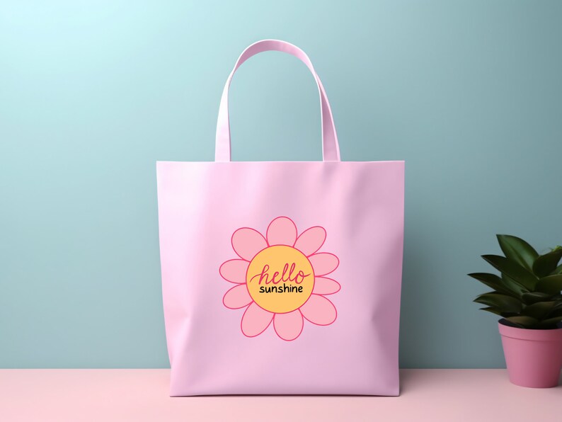 Op de afbeelding: Roze tote bag met een roze bloemetjesontwerp en de tekst "hello sunshine" in een gele cirkel.