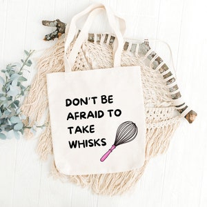 Puede incluir: Bolsa de tela blanca con texto negro que dice "No tengas miedo de tomar batidores". Un batidor rosa y negro est&aacute; ilustrado junto al texto.