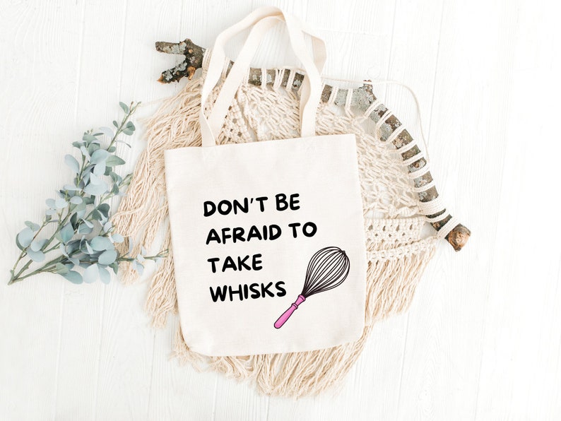 Puede incluir: Bolsa de tela blanca con texto negro que dice "No tengas miedo de tomar batidores". Un batidor rosa y negro est&aacute; ilustrado junto al texto.