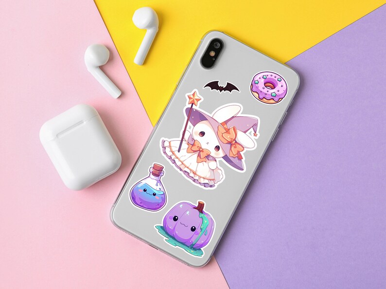 Puede incluir: Una funda de tel&eacute;fono blanca con una variedad de pegatinas de colores. Las pegatinas incluyen una dona morada y blanca, una calabaza morada, una botella de poci&oacute;n morada y un conejito blanco con un sombrero de bruja morado y una varita.