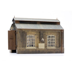 May include: A brown brick building with a grey roof and two windows. The building has a wooden door and a small pipe on the side.