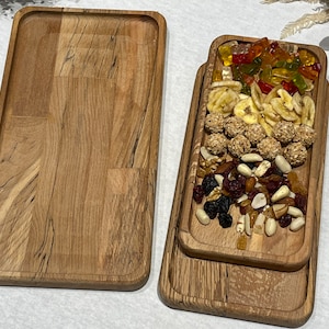 May include: Two wooden serving trays, one empty and one filled with a variety of snacks, including gummy sweets, banana chips, chocolate covered nuts, and dried fruit.