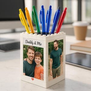 Puede incluir: Un portalápices blanco con el texto "Daddy & Me" y fotos de un padre y su hijo. El portalápices contiene bolígrafos de colores amarillo, naranja, verde, azul y rojo. Un corazón es visible en la parte delantera.