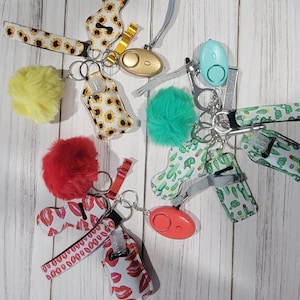 Può includere: Una collezione di portachiavi con vari design, tra cui girasoli, cactus, labbra e pompon. Ogni portachiavi include una piccola bottiglia per disinfettante per le mani e un allarme personale.