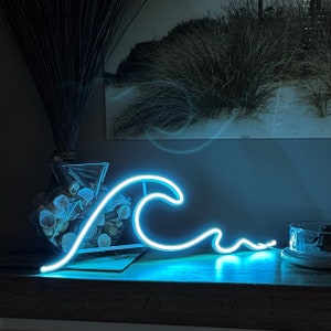 Puede incluir: Una luz de neón azul con forma de ola. La luz está sobre una superficie de madera y proyecta un brillo azul.
