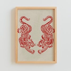 Puede incluir: Una impresión enmarcada con dos tigres estilizados rojos que se miran. Los tigres están delineados en negro y tienen un estilo japonés tradicional.