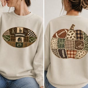May include: A beige crewneck sweatshirt featuring a patchwork football graphic on the front and a large patchwork pumpkin graphic on the back. The designs incorporate various brown, green, and cream patterns including plaid, stars, and football motifs.