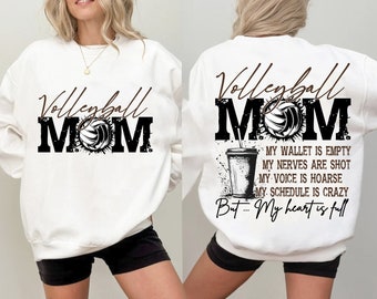 May include: White sweatshirt featuring the text "Volleyball MOM" in black and brown, with a volleyball graphic. The back of the sweatshirt has a volleyball graphic and the text: "My wallet is empty, my nerves are shot, my voice is hoarse, my schedule is crazy, but... My heart is full."