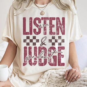 May include: A white t-shirt with a distressed red graphic that says "We Listen & We Don't Judge".