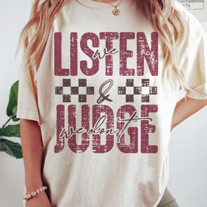 May include: A white t-shirt with a distressed red graphic that says "We Listen & We Don't Judge" with black and white checkered squares.