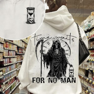 Può includere: Felpa con cappuccio bianca con una stampa grafica in bianco e nero di uno scheletro incappucciato che tiene una clessidra e una falce. Il testo "Time waits for no man" è stampato sotto la grafica.