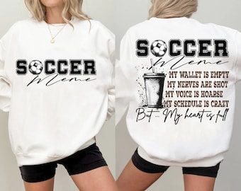 May include: White sweatshirt with black text that reads "Soccer Meme" and a soccer ball graphic. The back of the sweatshirt has the same text and graphic, along with a coffee cup graphic and the text "My wallet is empty, My nerves are shot, My voice is hoarse, My schedule is crazy, But... My heart is full."