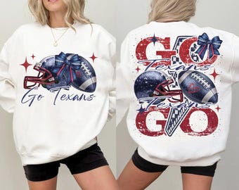 Puede incluir: Sudadera blanca con un diseño de casco y balón de fútbol americano. La parte delantera dice "Go Texans" en escritura azul. La parte trasera dice "Go Texans Go" en rojo y azul.