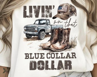 Puede incluir: Camiseta color crema con un diseño gráfico que presenta una camioneta vintage, botas de vaquero y una gorra de béisbol con una bandera estadounidense. El texto dice "LIVIN' on that BLUE COLLAR DOLLAR."