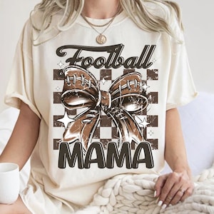 May include: A cream-colored t-shirt with a brown football-shaped bow and the text "Football Mama" on a checkered background.