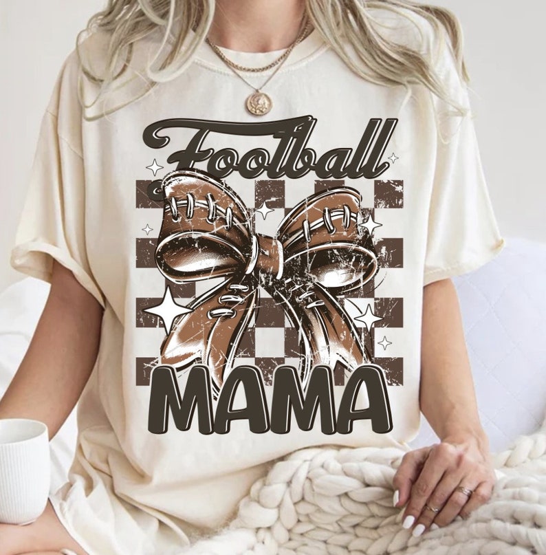 May include: A cream-colored t-shirt with a brown football-shaped bow and the text "Football Mama" on a checkered background.