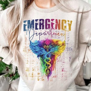 May include: A beige sweatshirt with the text "EMERGENCY Department" in rainbow colors. A colorful caduceus symbol with wings is centered on the shirt.