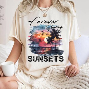 May include: A white t-shirt with a watercolor sunset graphic and the text "forever chasing sunsets".
