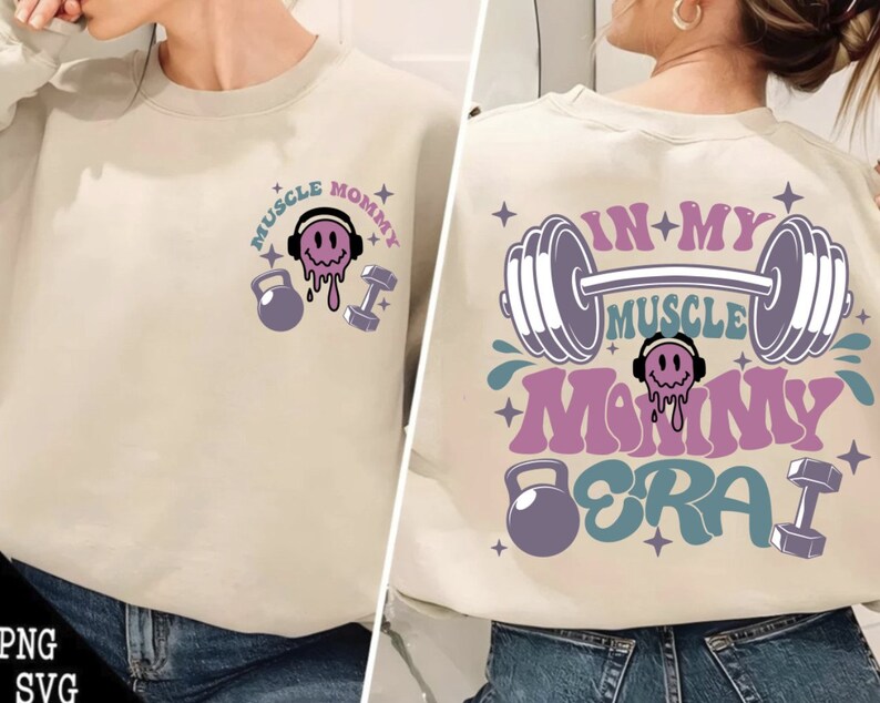 May include: A light beige sweatshirt with the text "Muscle Mommy Era" in pink, blue, and purple. The text is surrounded by dumbbells, a smiling face with headphones, and stars.
